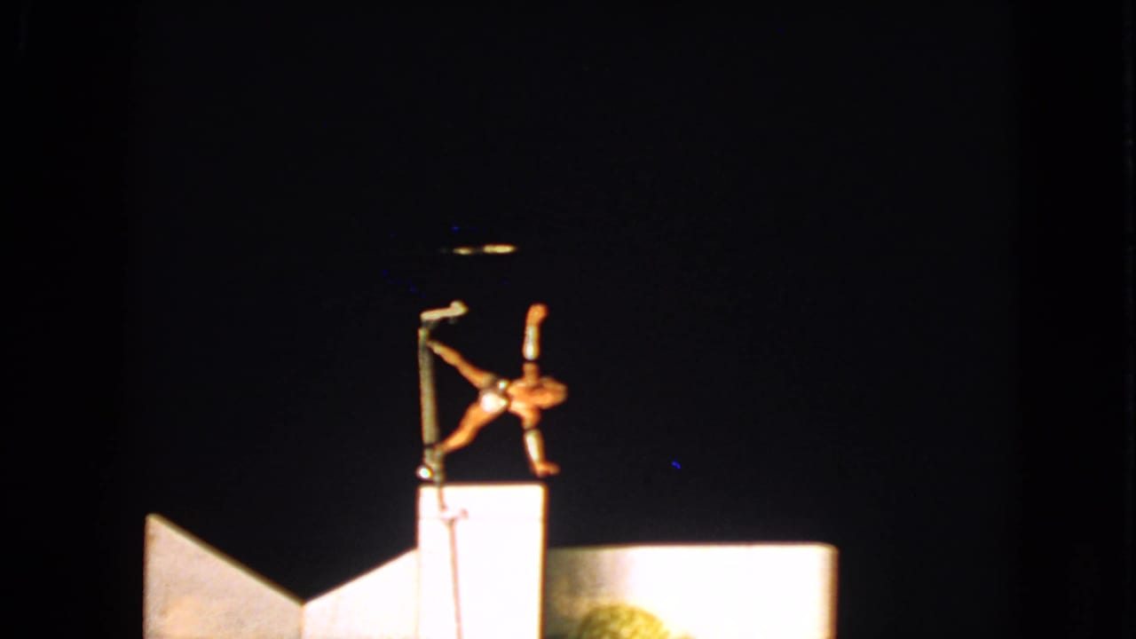1963 Walworth, Wisconsin 8mm frame with a performer inverted on a pole, lit by a strong spotlight over pale stage shapes.