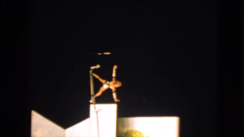 1963 Walworth, Wisconsin 8mm frame with a performer inverted on a pole, lit by a strong spotlight over pale stage shapes.
