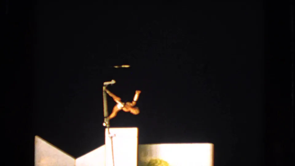 1963 Walworth, Wisconsin home-movie frame showing a pole acrobat in an angular pose over a brightly lit stage base.
