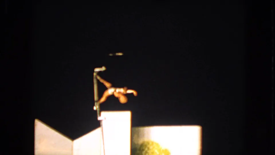 1963 Walworth, Wisconsin 8mm frame showing a spotlighted acrobat leaning outward from a pole during a nighttime act.