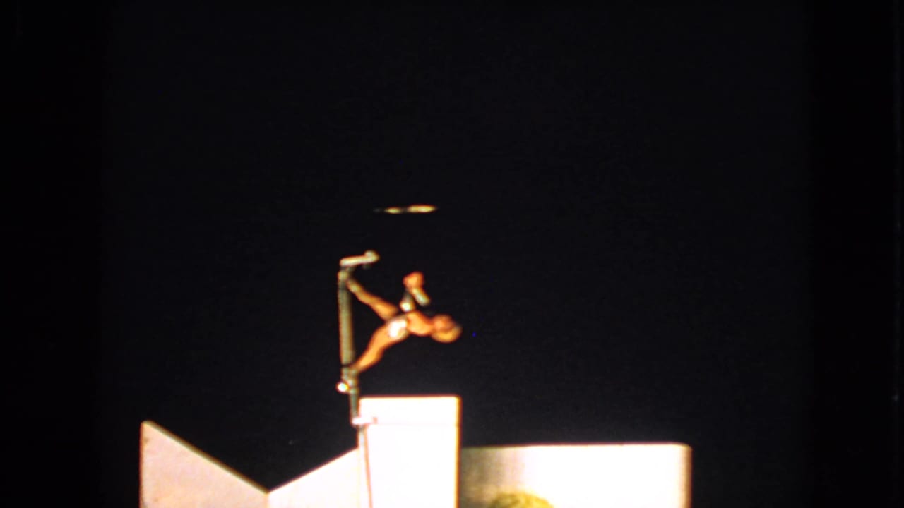 Female acrobat balances on a vertical pole above a lit platform against a dark stage.