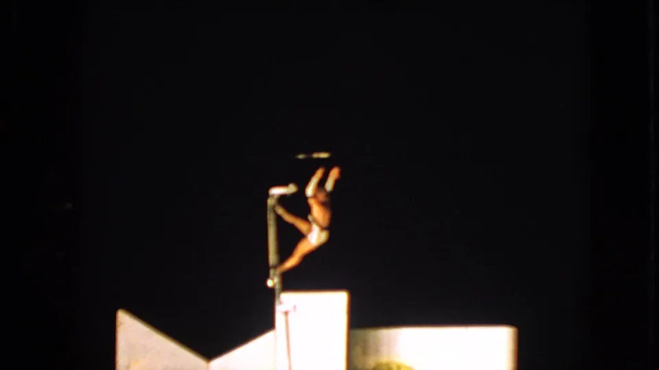 The 1963 8mm frame shows the acrobat changing position on the pole under strong stage lighting in Walworth, Wisconsin.