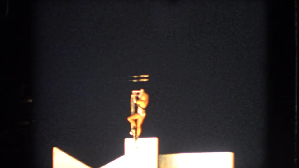 The closing frame shows the Walworth 1963 acrobat upright on the pole apparatus, centered against the dark stage backdrop.
