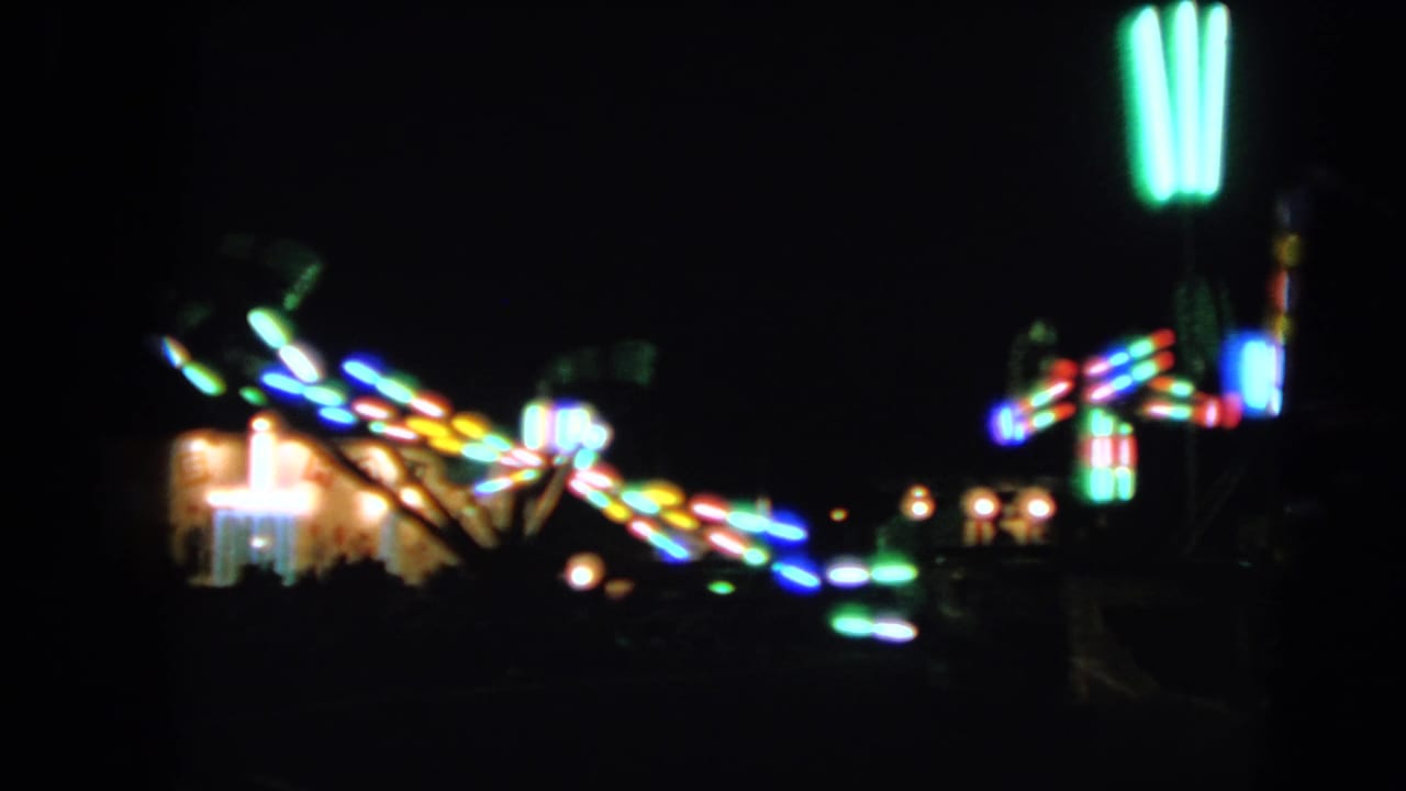 Out-of-focus fairground lights and ride structures at night.