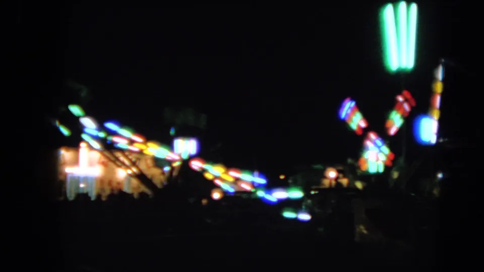1963 home-movie frame showing distant colorful carnival lights in Walworth, softened by motion blur and low light.