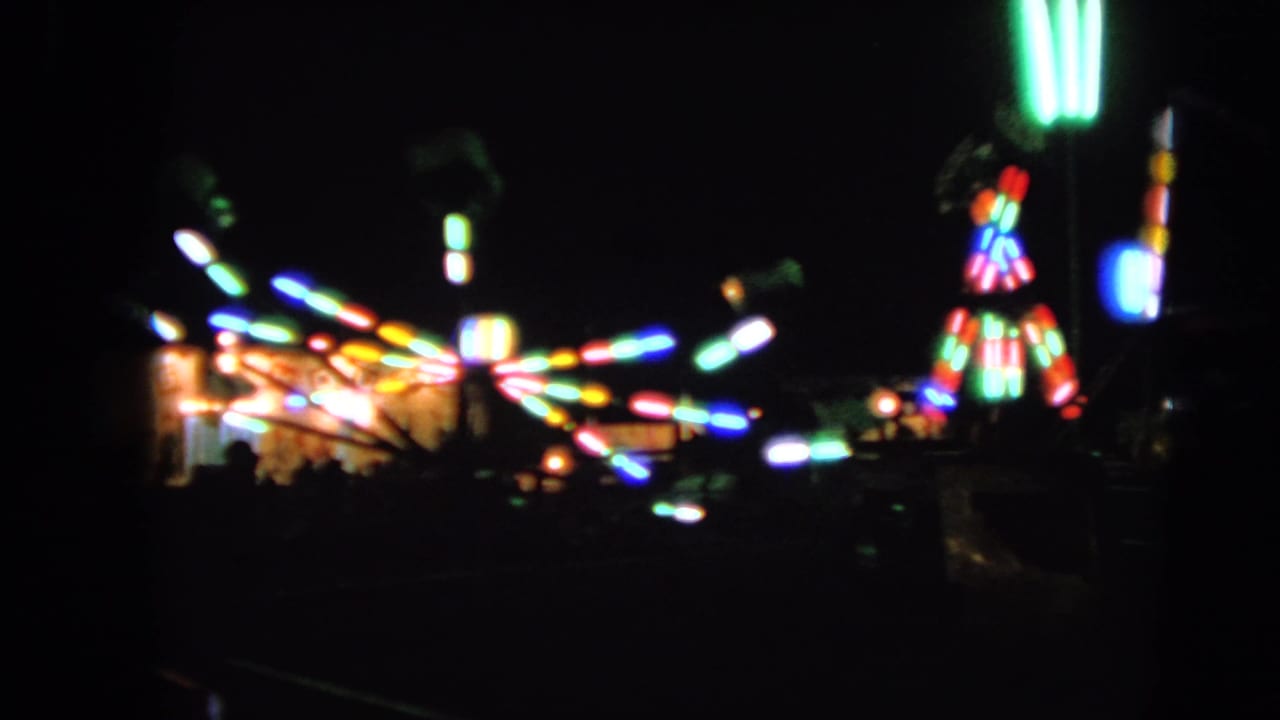 Bright carnival ride lights stretch across a dark fairground scene.