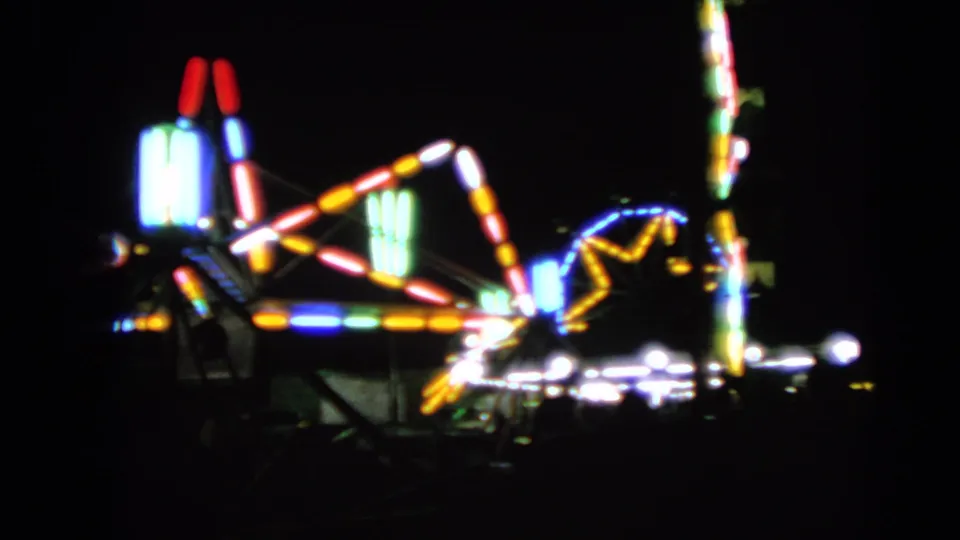 Walworth fair ride lights glow in soft focus, with colored arms, bright bulbs, and a vertical lighted pole against the night.