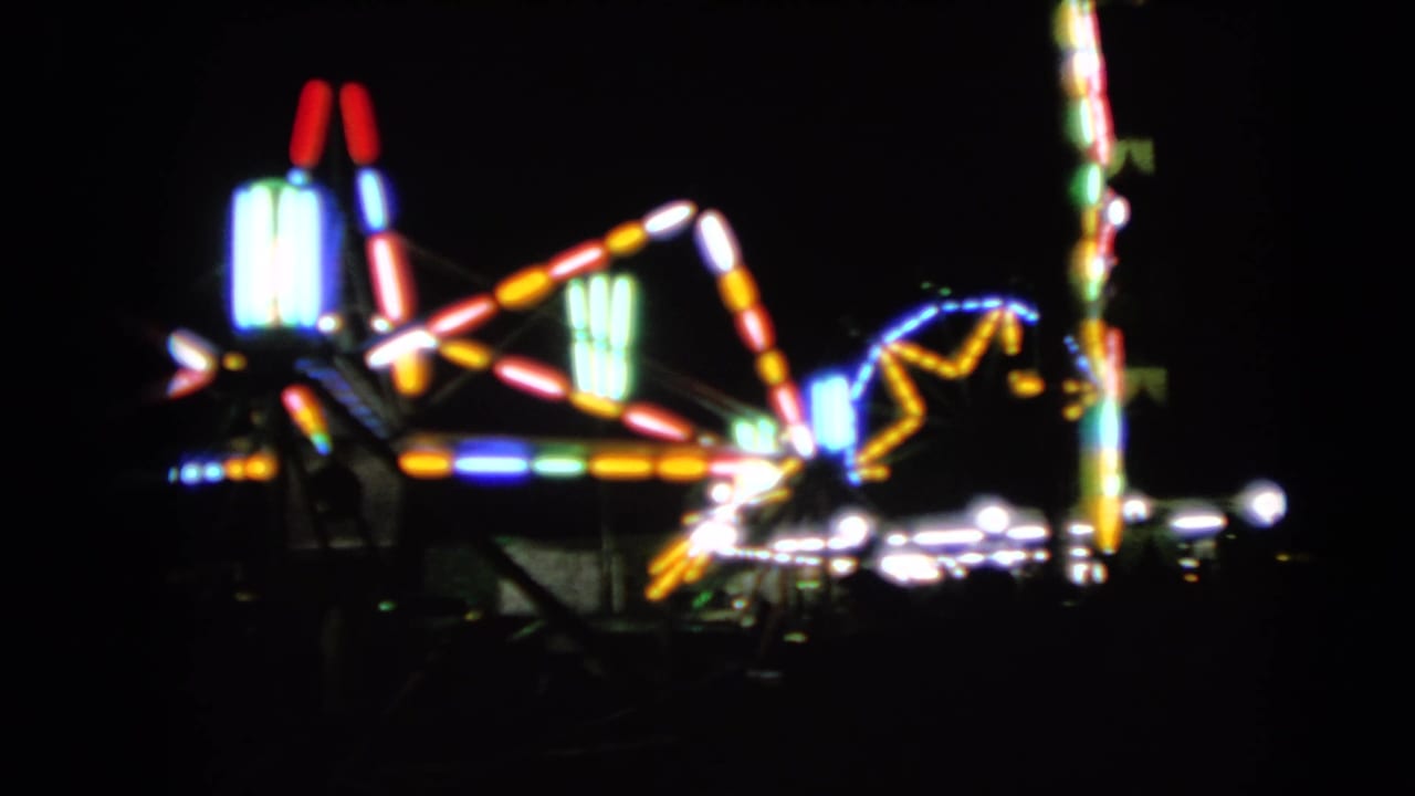 Out-of-focus 1963 home-movie frame of illuminated carnival ride structures at night in Walworth, Wisconsin.