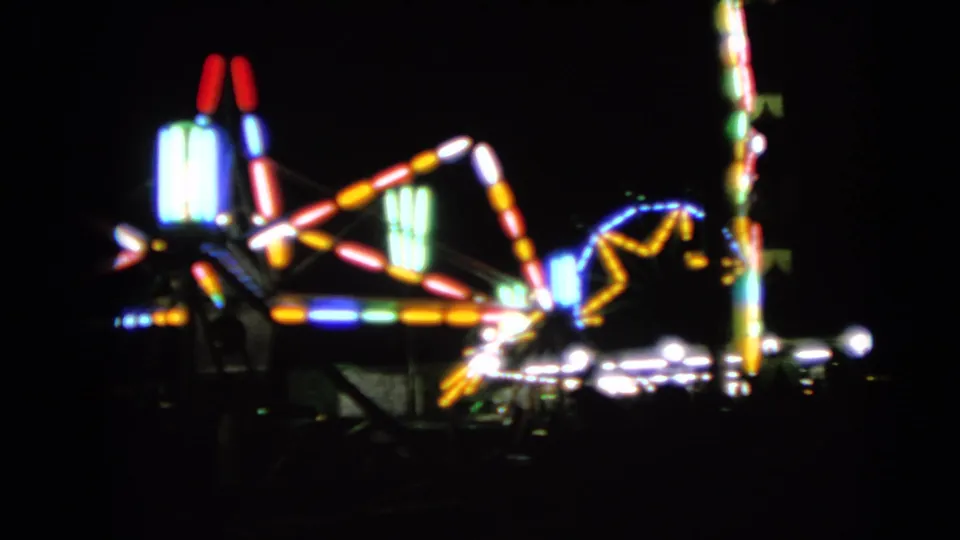 Out-of-focus 1963 home-movie frame of illuminated carnival ride structures at night in Walworth, Wisconsin.