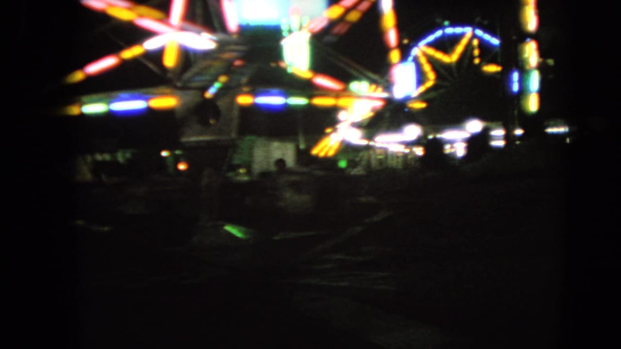 Blurred multicolored lights from a spinning carnival ride against a dark night sky.