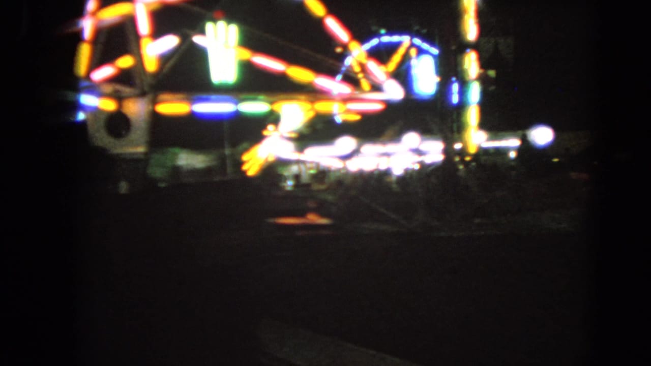 Bright carnival ride lights form streaks and arcs in a dark fairground scene.