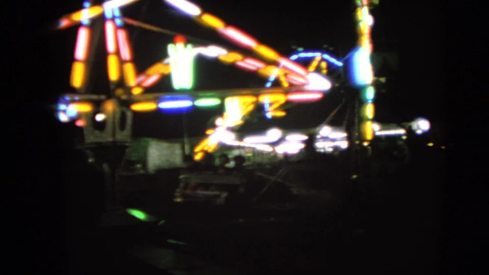 The 8mm frame shows a closer nighttime view of a spinning fair ride with colored bulbs and soft motion blur in Walworth, Wisconsin.