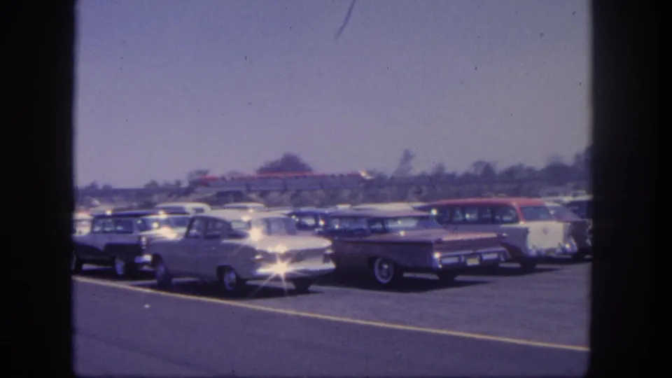 1962 Disneyland parking lot view with early-1960s cars, station wagons, lane markings, trees, and a distant red train in the background.