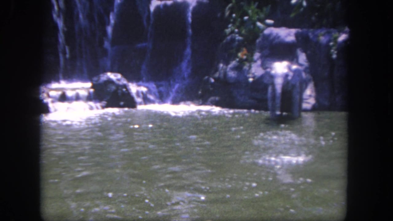 Waterfall and rocky pool enclosure with rippled water in the foreground.