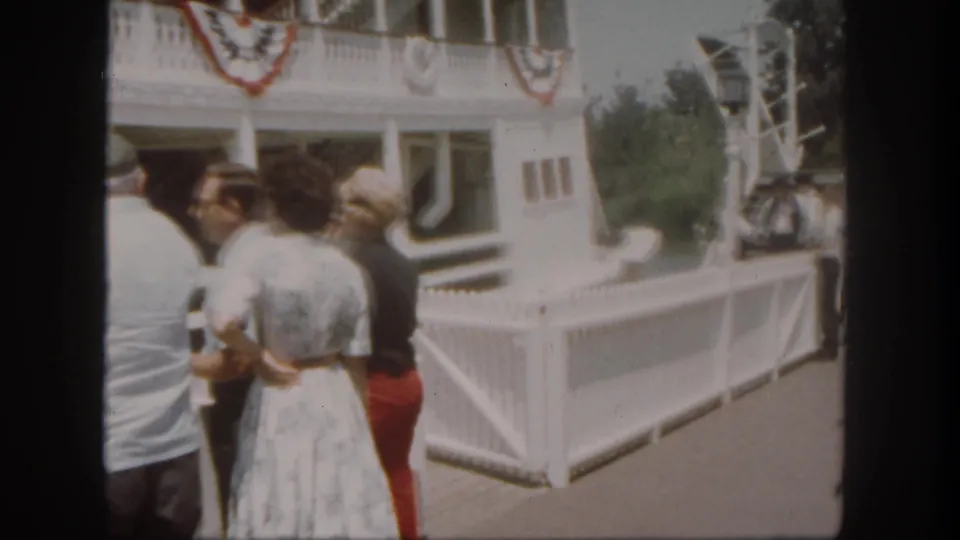 The handheld 8mm view follows adult visitors beside the white Disneyland dock fence and riverboat landing.
