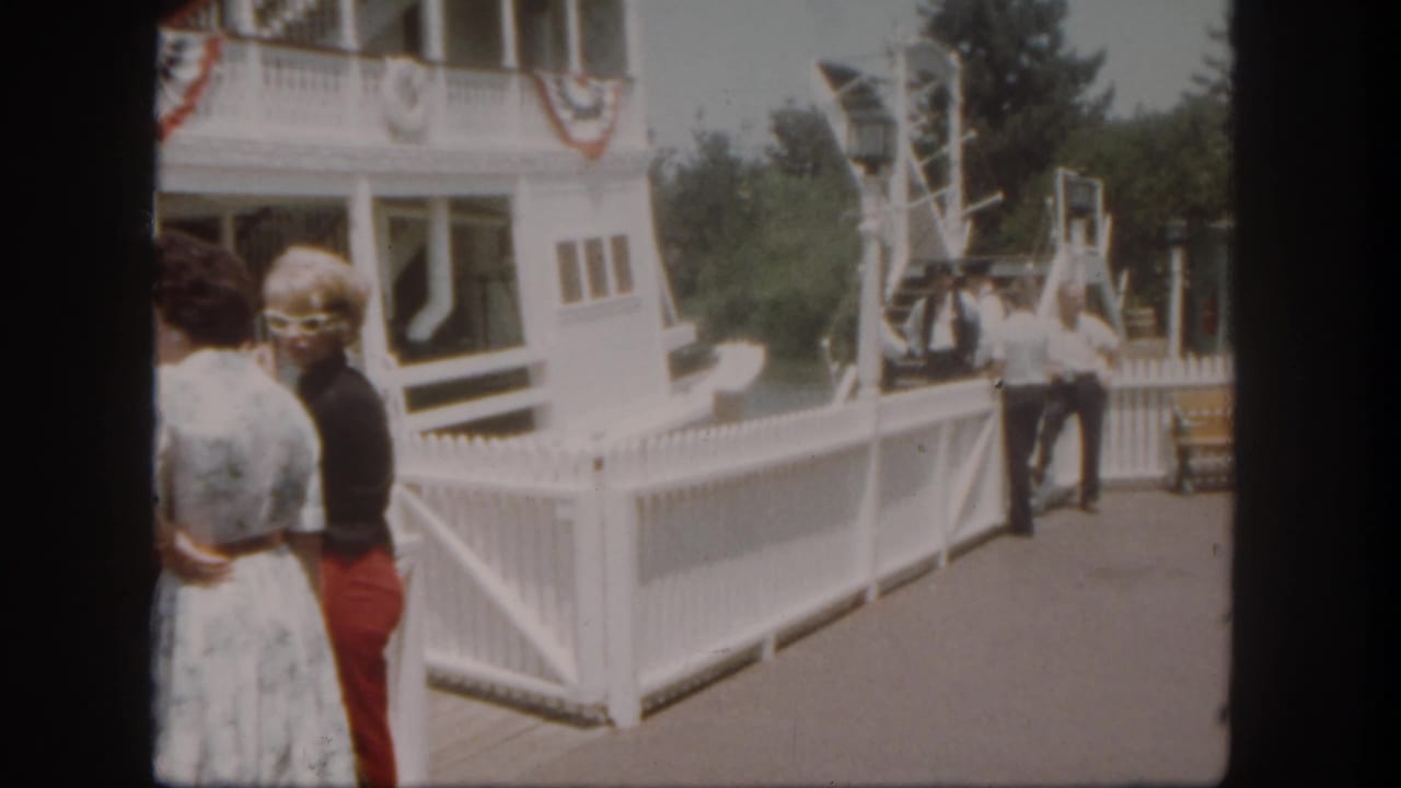 At Disneyland California in 1962, adult visitors stand near a white riverboat dock while crew members wait by the gangway.
