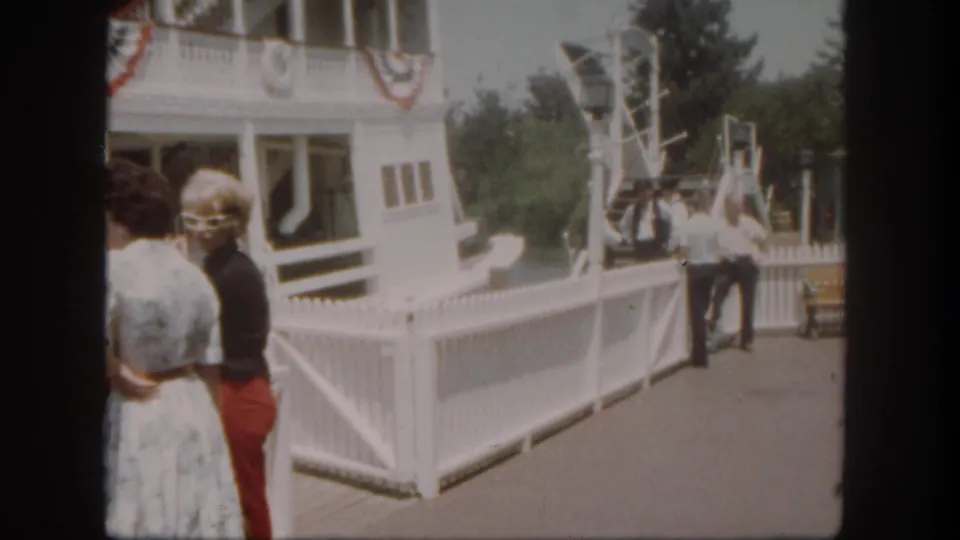 At Disneyland California in 1962, adult visitors stand near a white riverboat dock while crew members wait by the gangway.