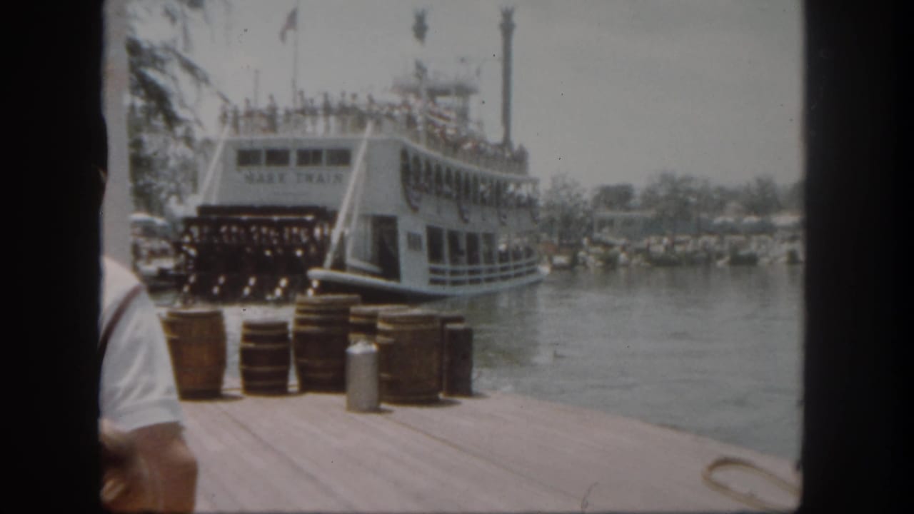 Mark Twain riverboat docked with guests aboard and barrels on the pier.