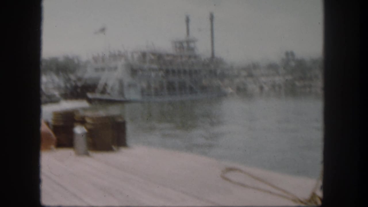 The Disneyland paddlewheel boat appears farther out on the water, with passengers visible and dock items partly framing the foreground.
