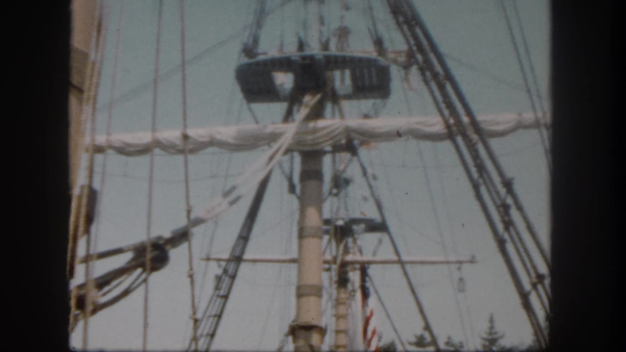 Ship mast, rigging, crow's nest, trees, and a partly visible American flag.