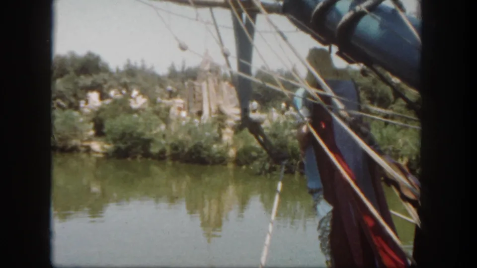 Visitor-shot 1962 Disneyland boat ride view with rigging close to the camera and trees reflected in the water.