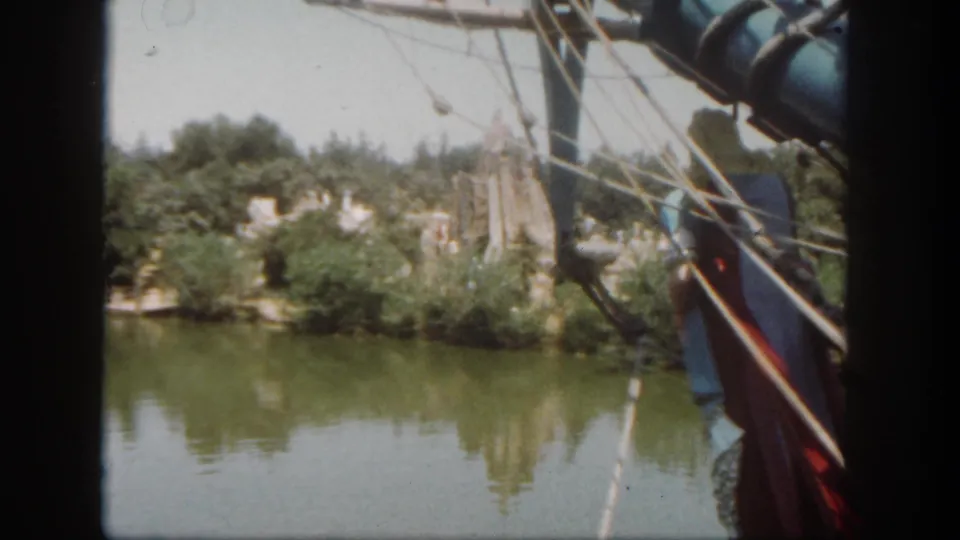 1962 Disneyland boat ride frame looking across calm water from beside rigging toward trees and constructed shoreline scenery.
