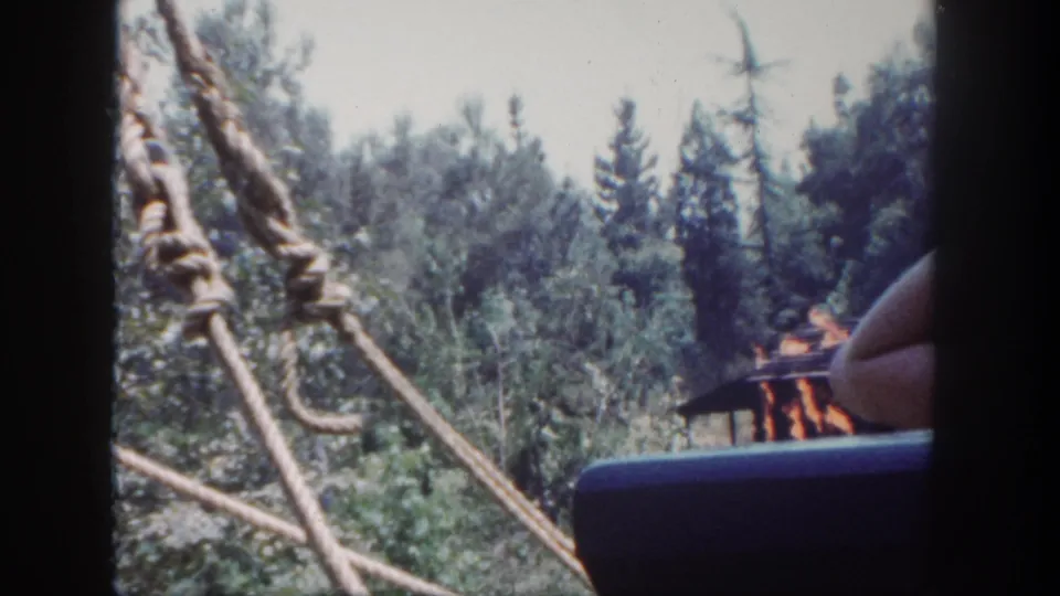 1962 Disneyland ride footage shows rope rigging, wooded scenery, a partial passenger, and a staged fire effect near a small structure.