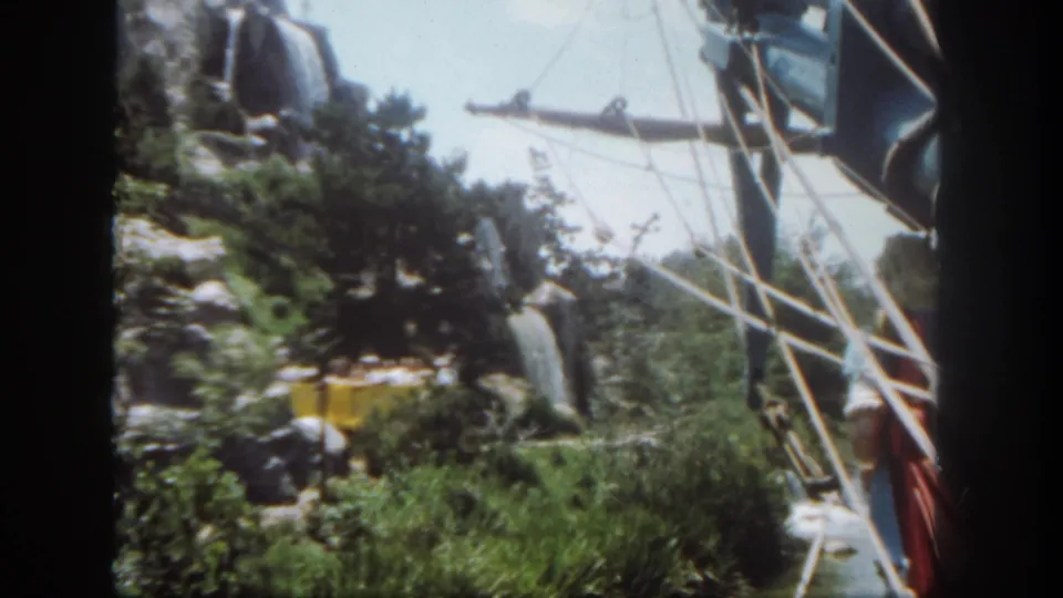 Final 1962 Disneyland frame shows the yellow passenger tram partly obscured by greenery, rockwork, and ride supports.