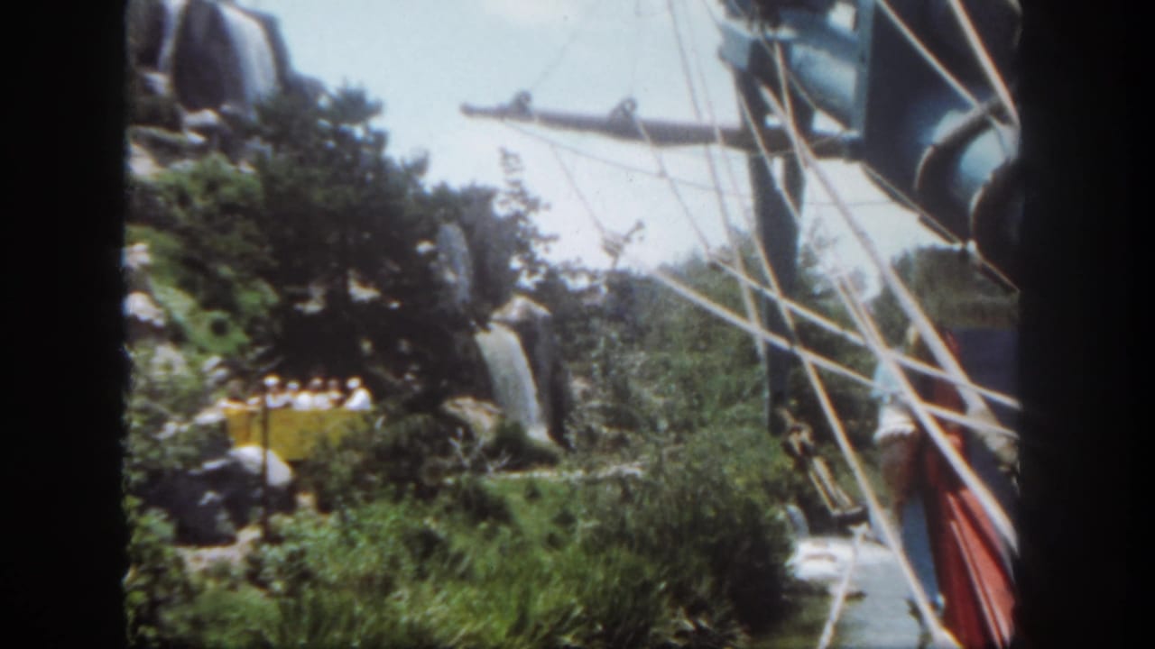 Pirate ship rigging passes greenery and waterfall scenery on a water ride.