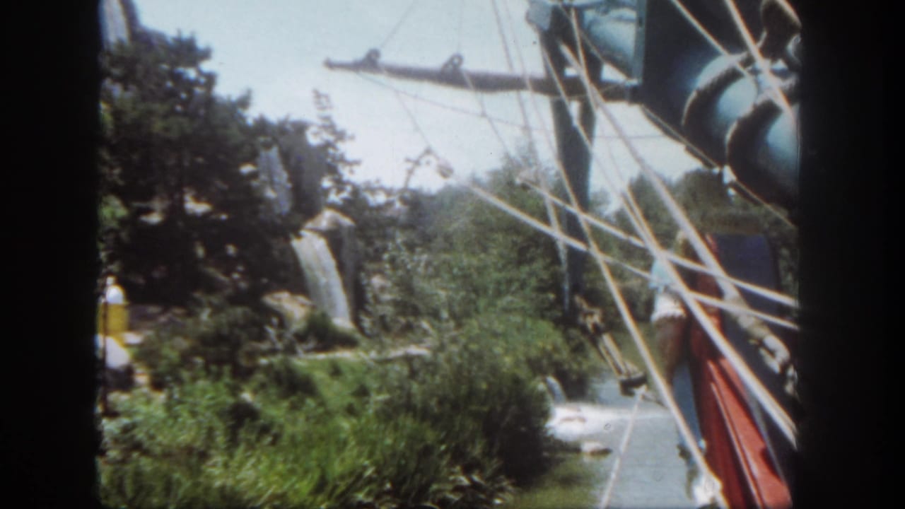 Water ride scenery with ship rigging, shrubs, rockwork, and a visible visitor.