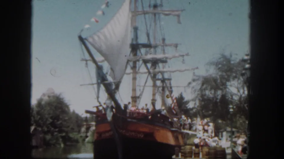 Soft 8mm frame of the Disneyland sailing ship attraction, with rigging, water, trees, and guests visible.