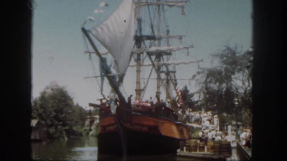 1962 Disneyland frame showing the ship attraction from a visitor viewpoint, with guests, trees, water, and sky.