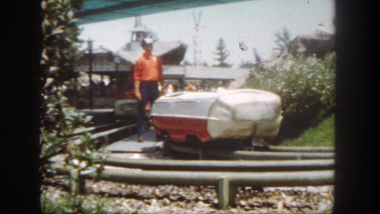 Attendant standing beside a red-and-white ride vehicle on an outdoor track.