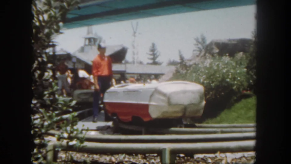 1962 Disneyland home-movie view of an attendant and ride vehicle, with visitors partly visible near the pavilion area.