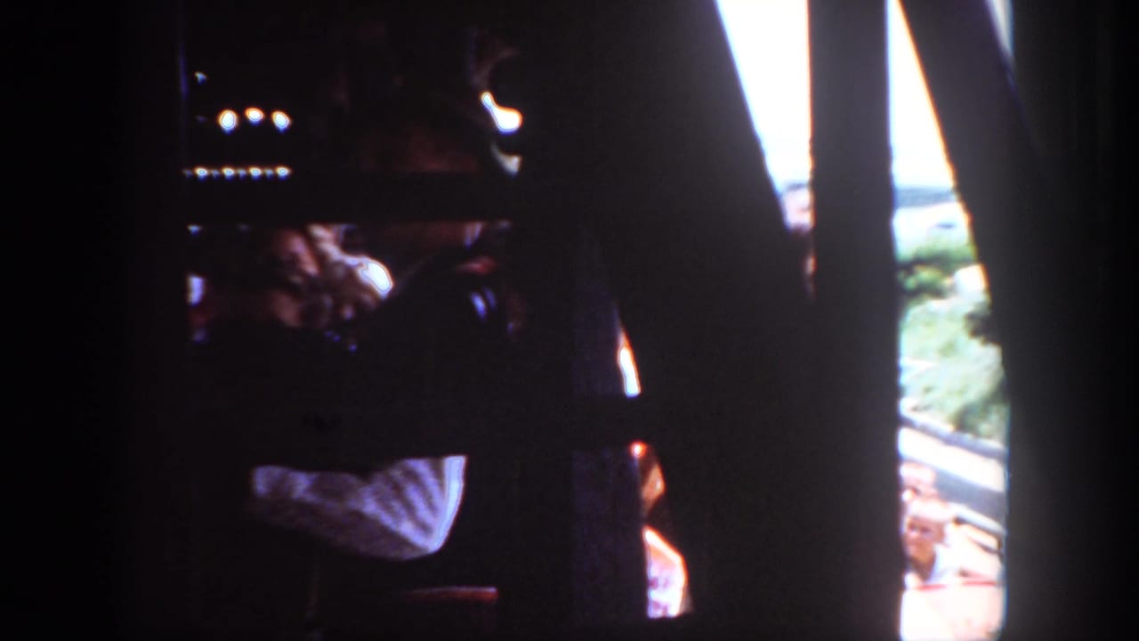 1962 Disneyland home-movie frame with dark projection borders, audience silhouettes, and a bright glimpse of the accordion performer outdoors.