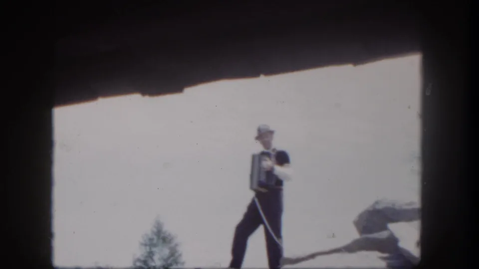 A visitor-shot 1962 Disneyland frame catches the accordion player mid-stance on a rocky ledge.