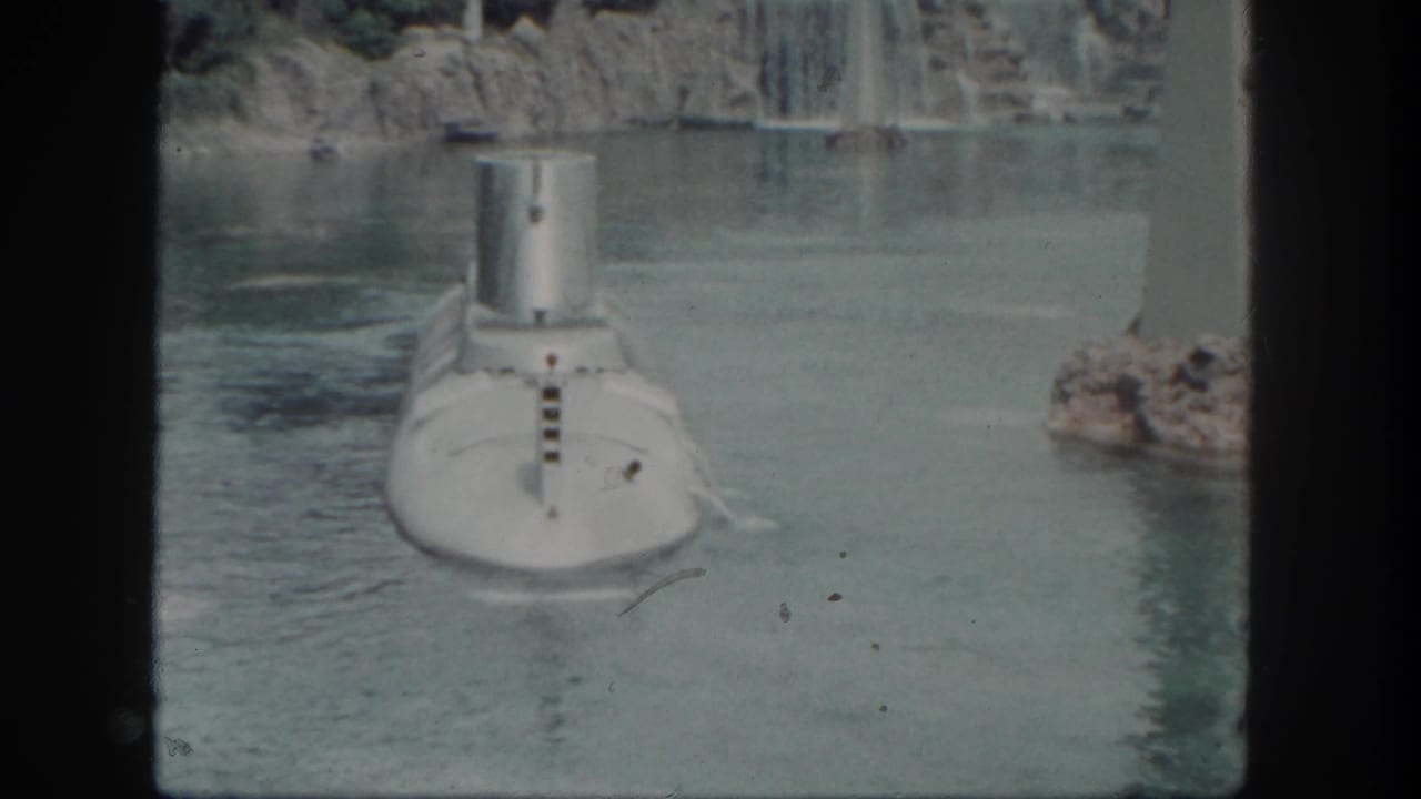 White submarine moving through a lagoon near rocks, waterfall, and a tall white pillar.