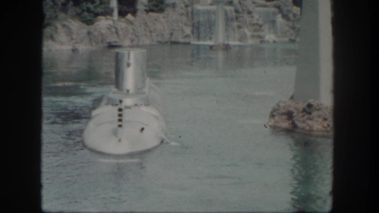 The Disneyland submarine appears slightly farther along the lagoon, framed by rock scenery, falling water, and a vertical white pillar.