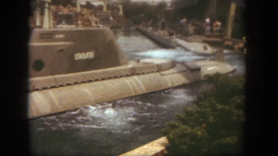 Close 8mm view of the SKATE submarine’s tower, portholes, and hull moving past the camera in the Disneyland ride channel.