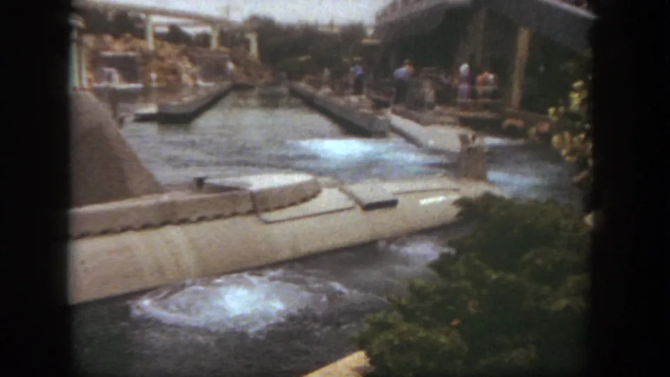Later frame from the 1962 Disneyland ride view, with the submarine’s rear section moving away through foamy canal water near foliage and guests.