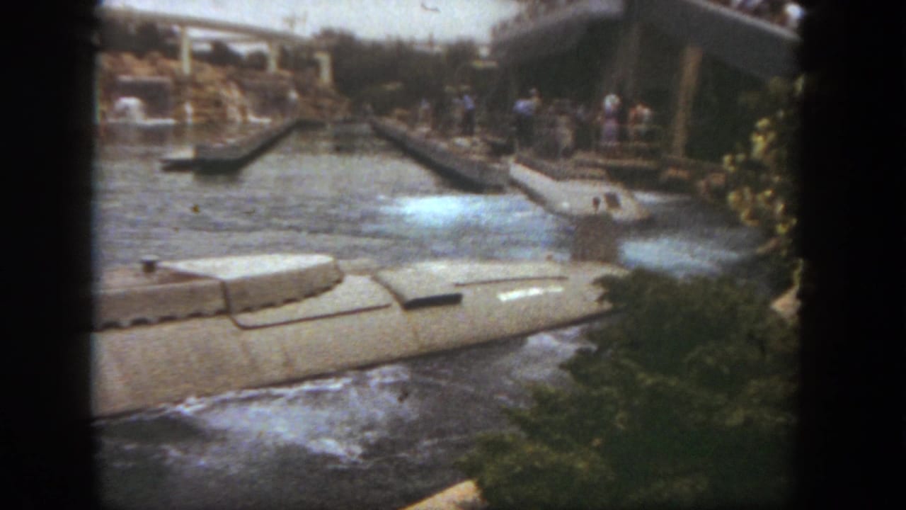 Submarine ride boat passing through a water channel with bridges, greenery, and guests in the background.