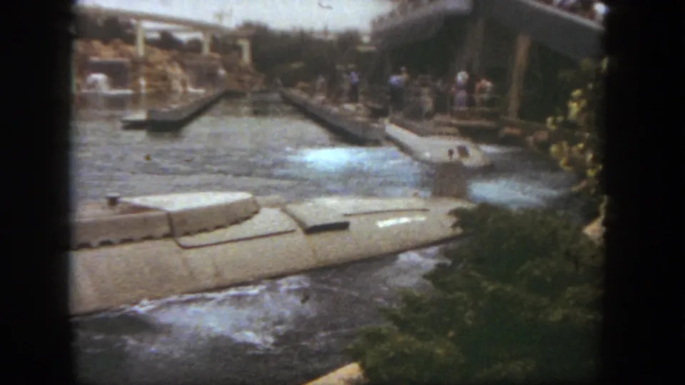 1962 Disneyland Submarine Voyage view with a submarine-style boat moving through water below arched bridges and distant guests.