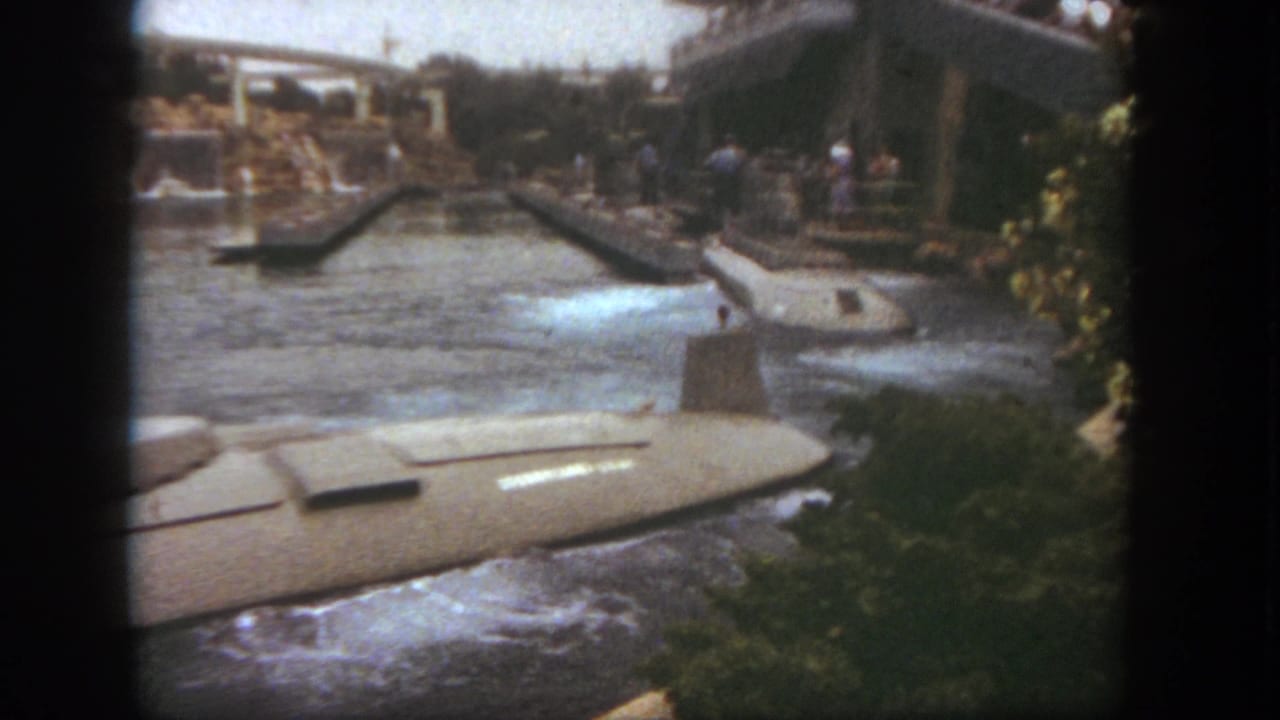 Submarine ride vehicle in the foreground with water turbulence, bridges, and guests near the loading area.