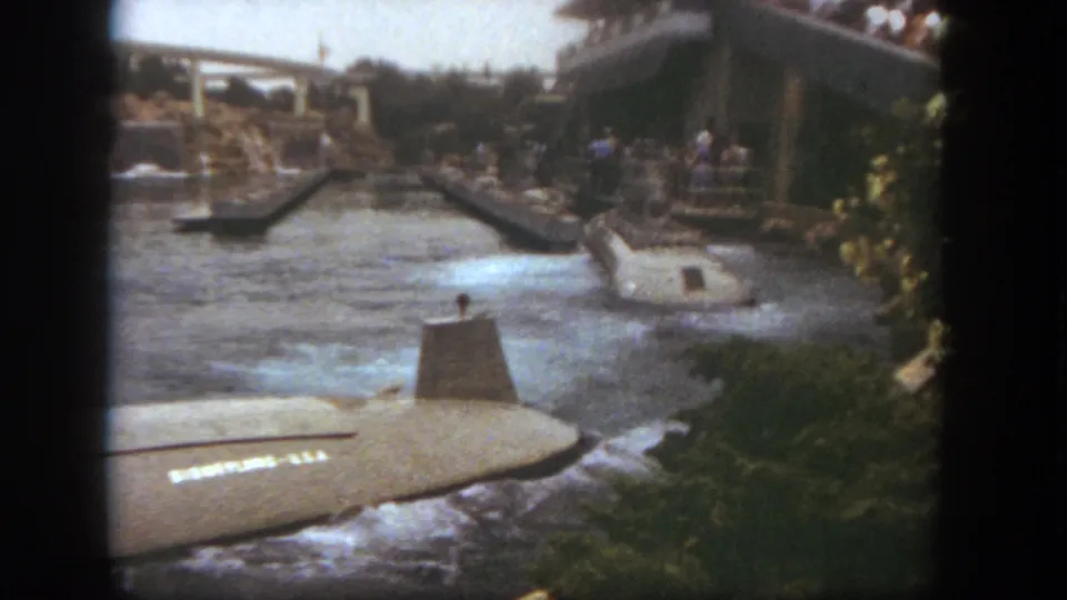The foreground submarine-style boat turns through the channel while another ride vehicle appears near the platform at Disneyland.