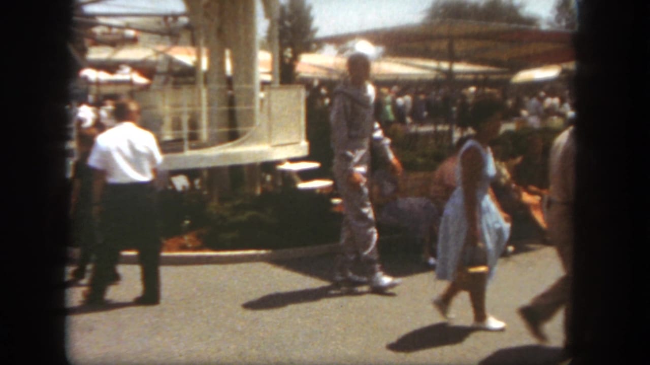 At Disneyland in 1962, visitors pass a man in a spacesuit costume on a bright park walkway.