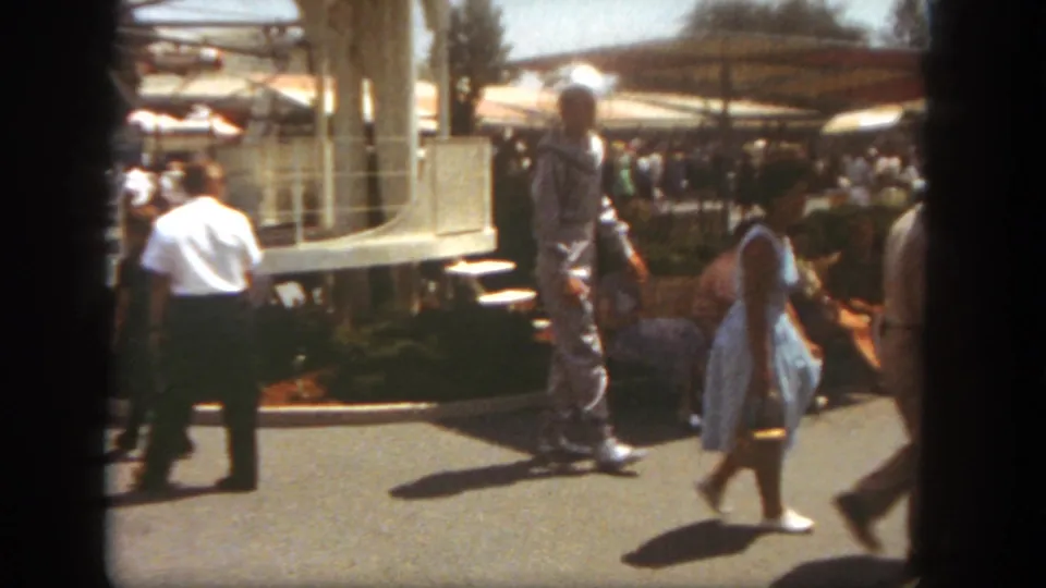At Disneyland in 1962, visitors pass a man in a spacesuit costume on a bright park walkway.