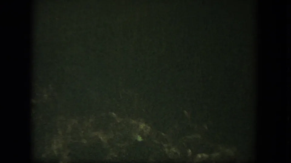 A dark, grainy transitional 8mm frame with faint green tones and indistinct lower-edge detail.