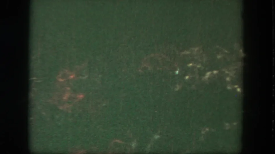 A dark 8mm frame with green cast, heavy grain, and indistinct reddish highlights toward the lower half.