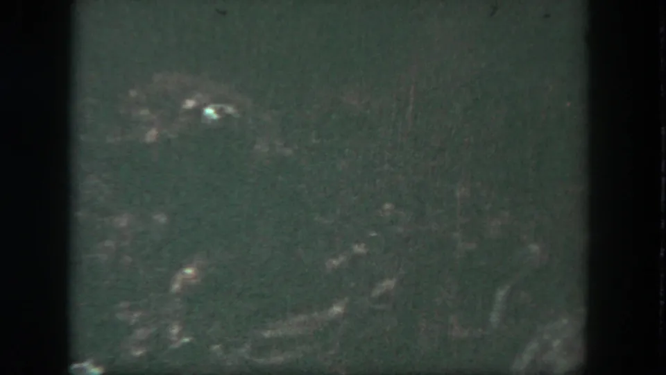Dim 1962 Disneyland frame with murky green water, faint underwater forms, and isolated bright reflections.