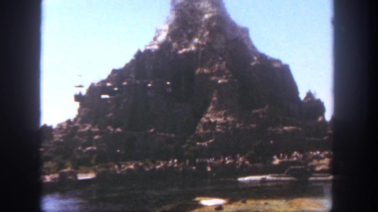 1962 Disneyland view of the Matterhorn area with suspended cable cars, water, small boats, and distant visitors.